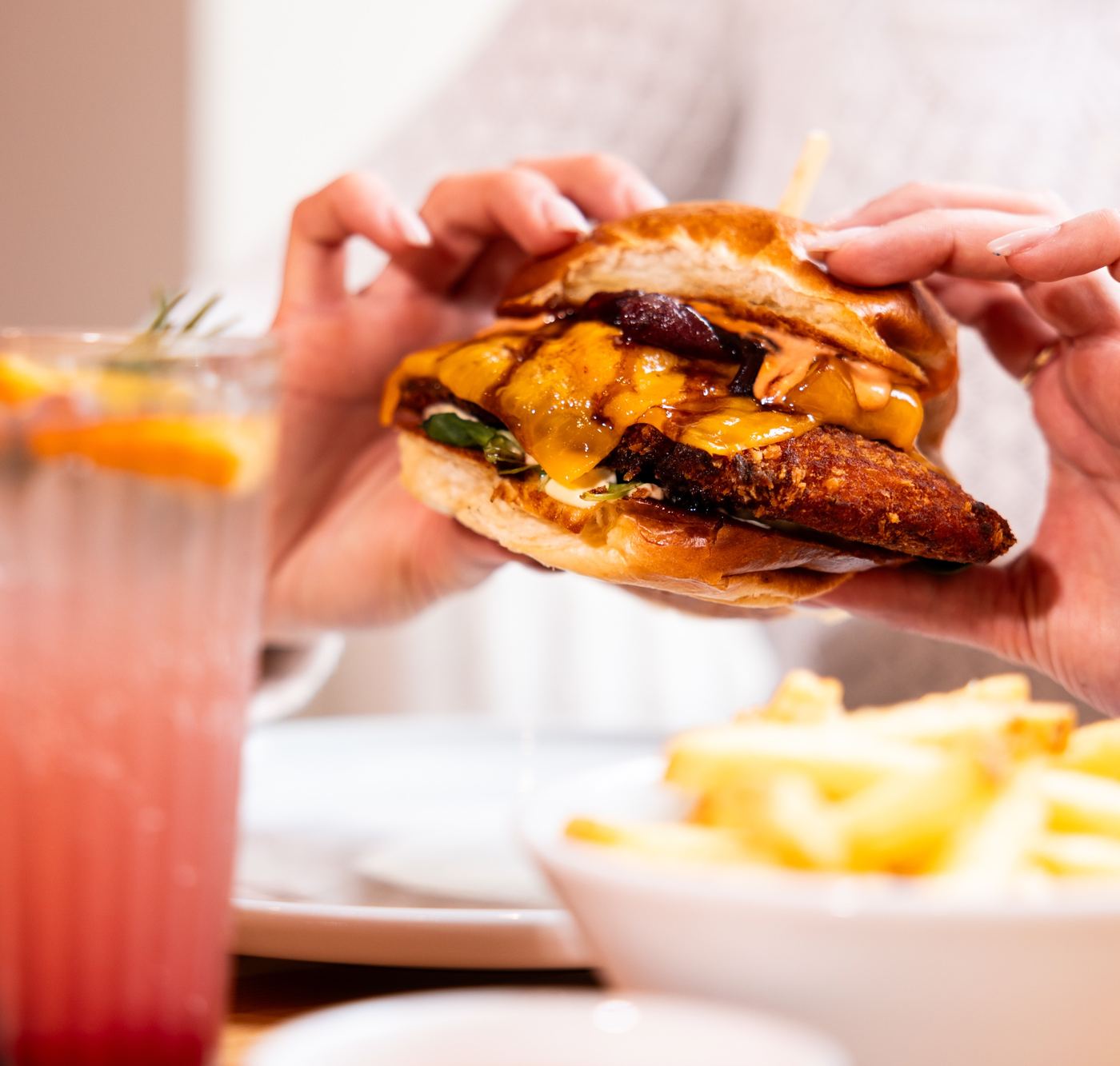 Host drží crispy chicken burger, vedle růžová limonáda a hranolky
