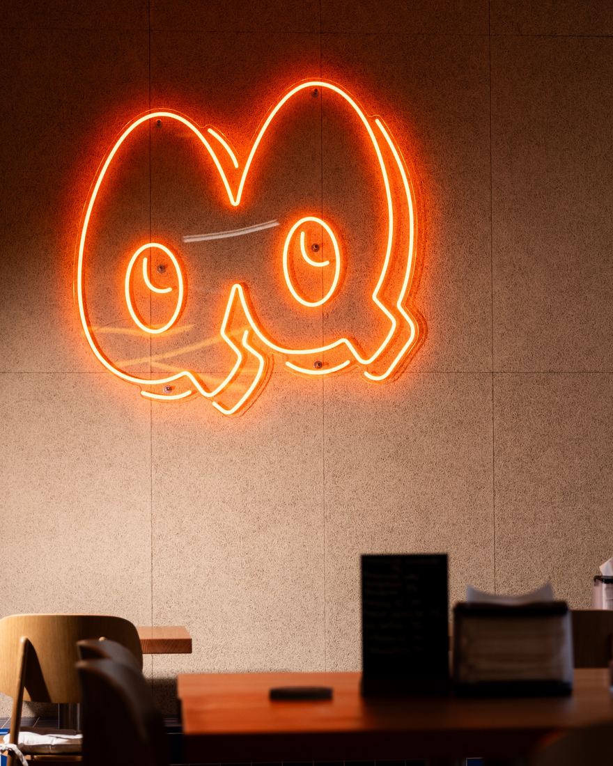 Oranžový neon QUOQ s očima na stěně uvnitř bistra